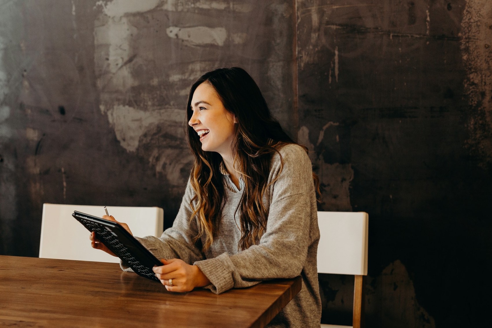 A woman smiling as she looks at a tablet at a wooden table