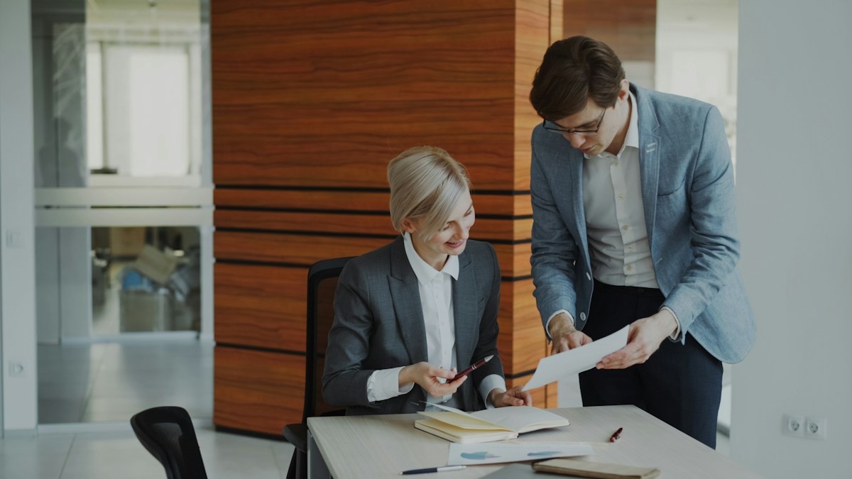 A colleague handing a document to a coworker at a desk